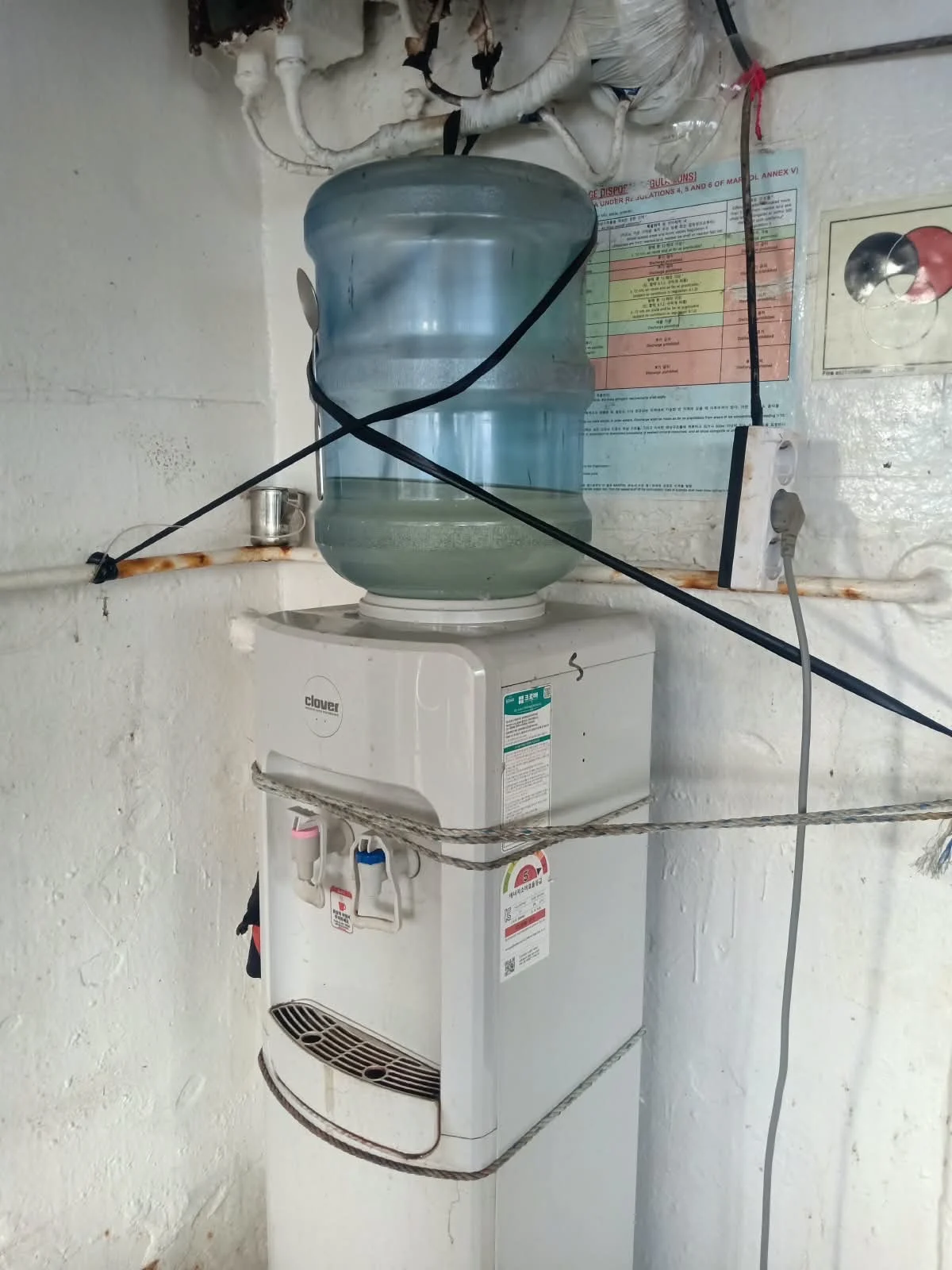 Galon di atas dispenser yang diikat pada sekat