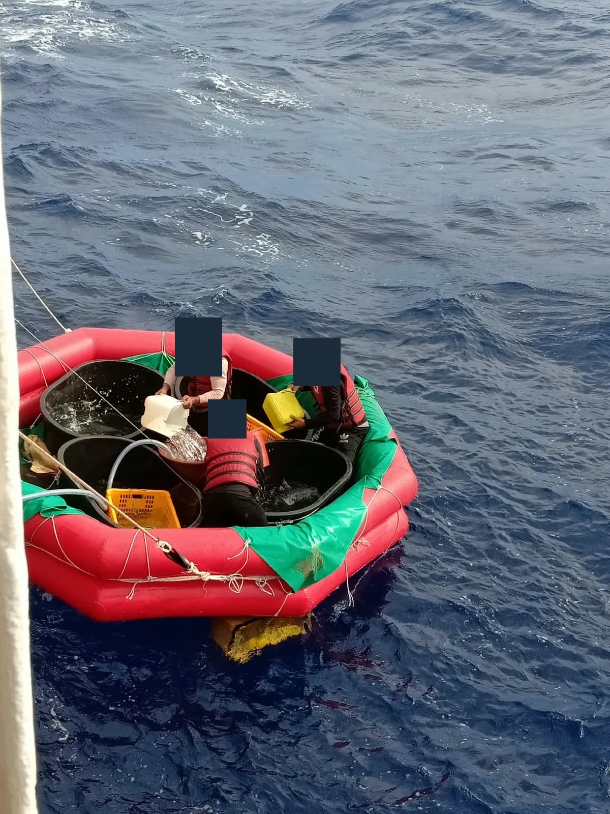 Tiga orang memindahkan wadah dari perahu karet di sisi kapal